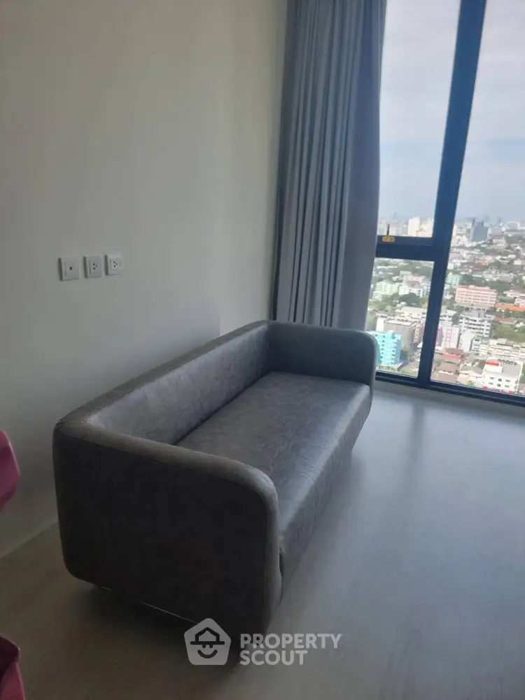 Modern living room with sleek sofa and panoramic city view through large window.
