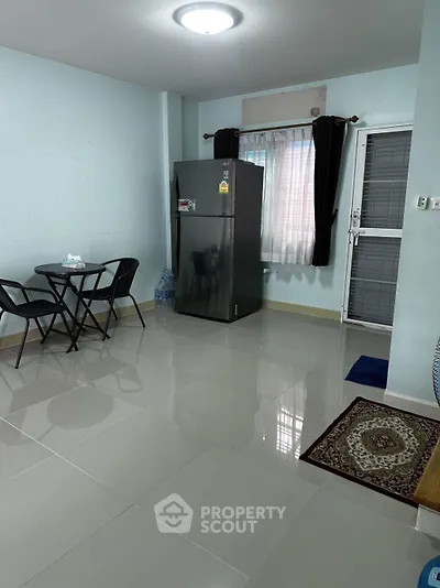 Cozy apartment interior with dining area and fridge, featuring tiled flooring and natural light.