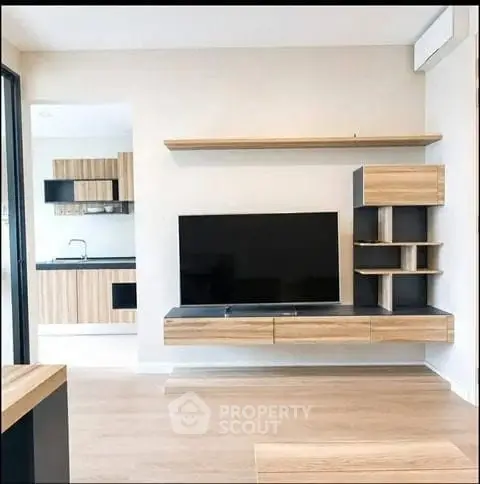 Modern living room with sleek TV unit and open kitchen layout, featuring contemporary wooden cabinetry.