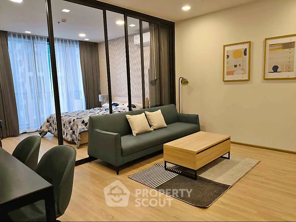 Modern open-layout living room with glass partition to bedroom, featuring stylish furniture and decor.
