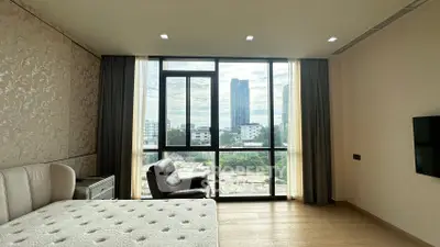 Spacious bedroom with floor-to-ceiling windows offering stunning city views, elegant decor, and modern furnishings.