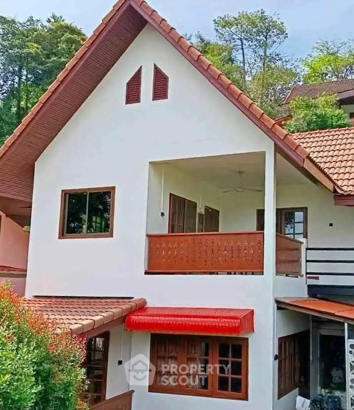 Charming two-story house with red-tiled roof and lush greenery, perfect for serene living.