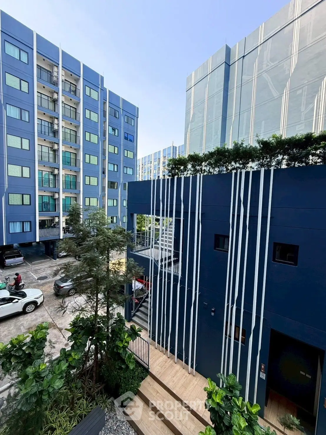 Modern apartment complex with blue facade and lush greenery in urban setting