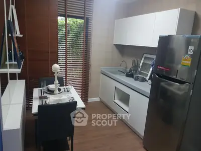 Modern kitchen with sleek cabinets and dining area, featuring a stainless steel fridge and stylish decor.