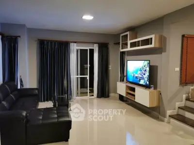 Modern living room with sleek black leather sofa and large TV, featuring elegant curtains and stylish shelving.