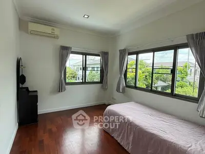 Bright bedroom with wooden floors and large windows offering lush garden views.