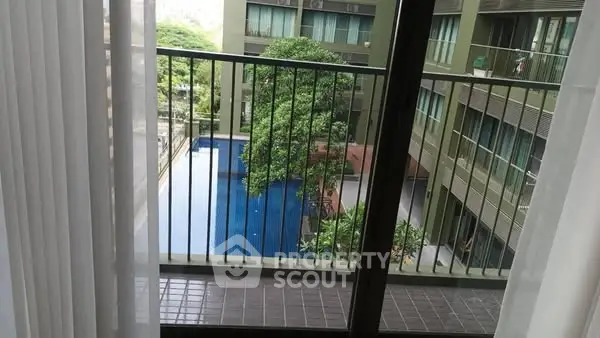 Modern apartment balcony overlooking a serene pool and lush greenery.