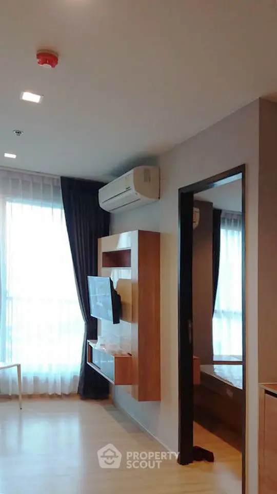 Modern living room with sleek wooden TV unit and large window with curtains.