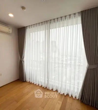 Bright room with large window and elegant curtains, featuring wooden flooring and air conditioning.