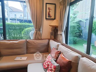 Cozy living room with large windows overlooking a lush garden, featuring a comfortable sofa and stylish decor.