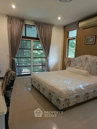 Spacious bedroom with elegant decor and large windows overlooking greenery, featuring a stylish bed and luxurious curtains.