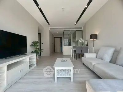 Modern living room with sleek furniture and open layout, featuring a large TV and stylish decor.
