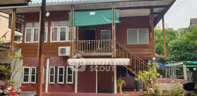 Charming two-story wooden house with balcony and lush greenery, perfect for serene living.