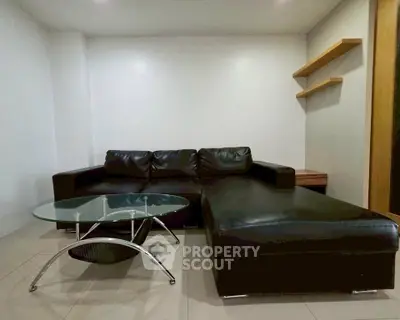 Modern living room with sleek black leather sectional and glass coffee table.
