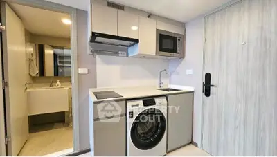 Modern compact kitchen with integrated washing machine and microwave in sleek apartment.