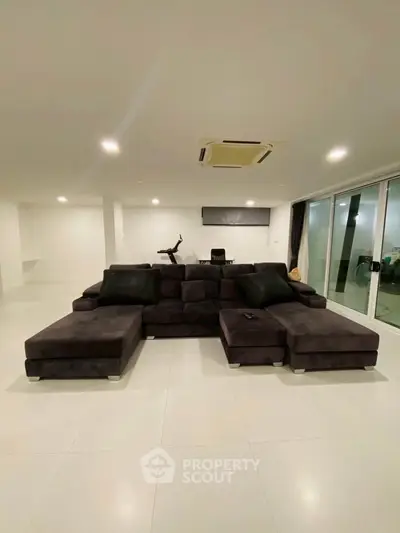 Spacious modern living room with sleek black sectional sofa and large windows for natural light.