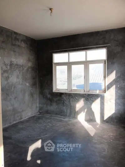 Spacious unfinished room with large window and concrete walls, ideal for customization.