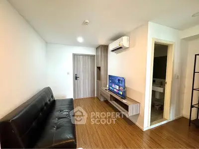 Modern living room with sleek black sofa, wall-mounted TV, and wooden flooring in a cozy apartment.