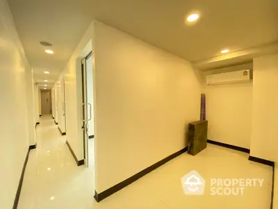 Spacious and well-lit corridor inside a modern residential building, featuring gleaming white walls and elegant black trim.