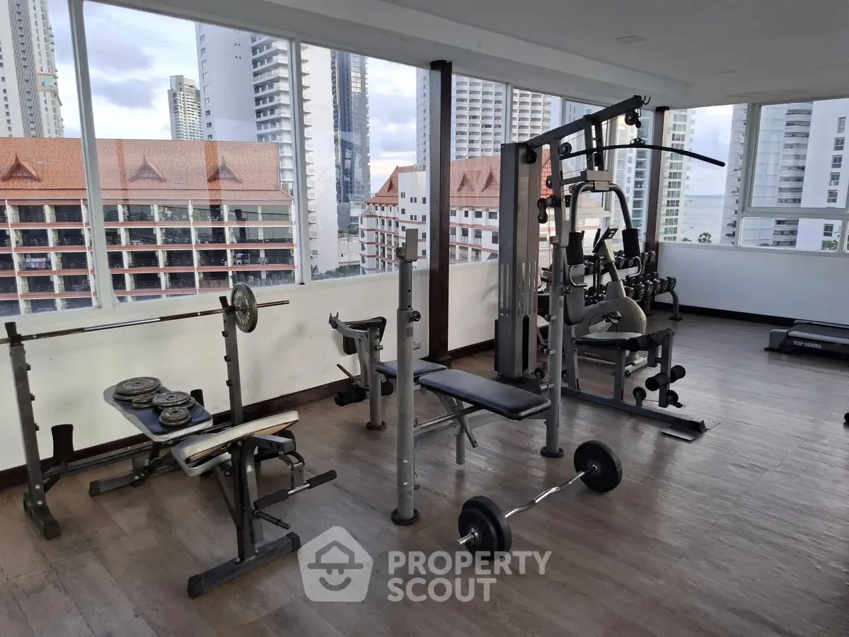 Spacious gym with modern equipment and city view in luxury apartment building.
