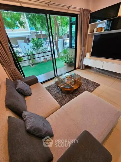 Modern living room with large glass doors opening to a lush garden view, featuring a cozy sectional sofa and sleek entertainment unit.