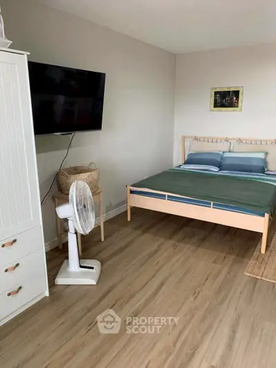 Cozy bedroom with wooden flooring, modern bed, and wall-mounted TV for a comfortable living space.