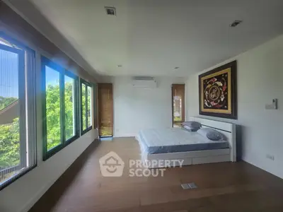 Spacious bedroom with large windows and serene view, featuring modern decor and wooden flooring.