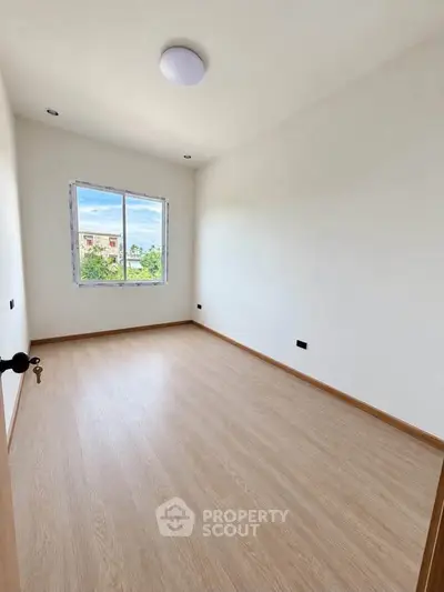 Spacious empty bedroom with large window and wooden flooring, perfect for customization.