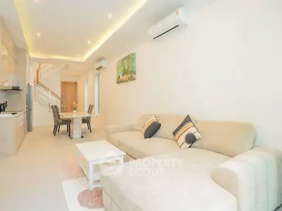 Spacious modern living room with open kitchen and elegant dining area, featuring cozy beige sofa and stylish decor.