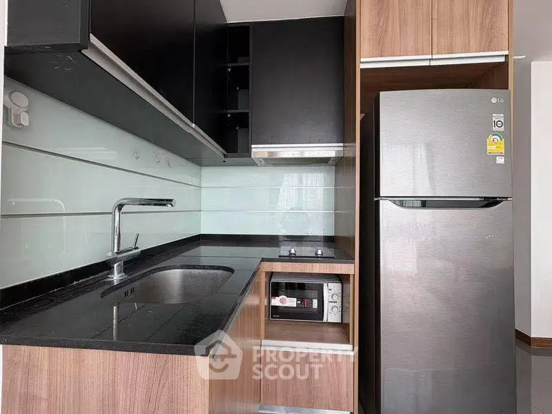 Modern kitchen with sleek black countertops and stainless steel appliances in a stylish apartment.