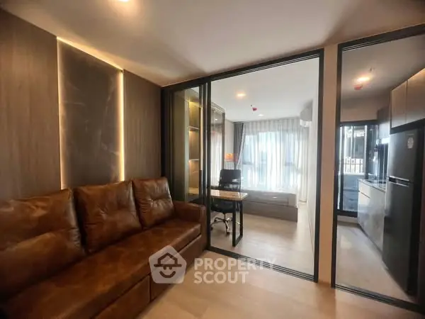 Modern living room with leather sofa and glass partition leading to study area.
