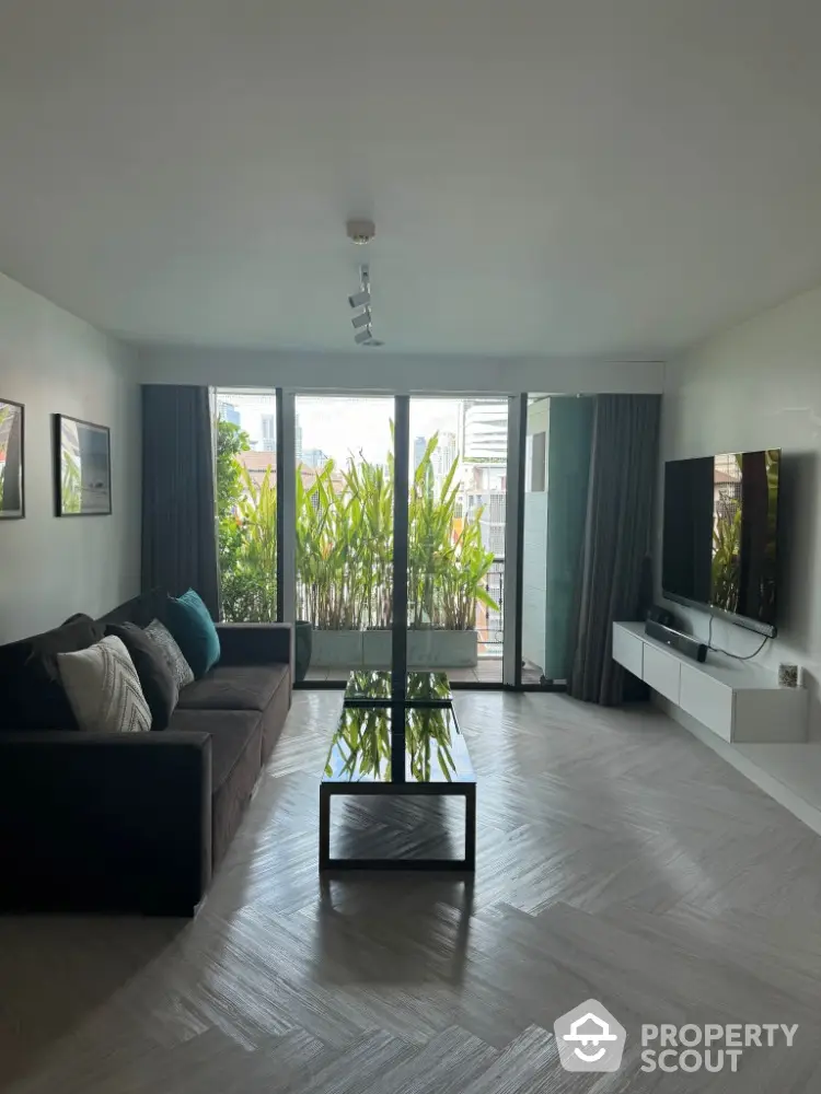 Spacious living room with modern decor and large windows opening to a lush balcony view.