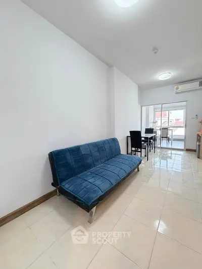 Modern living room with sleek blue sofa and dining area in open layout apartment.