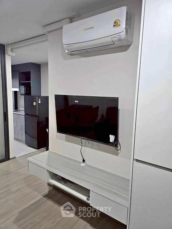 Modern living room with wall-mounted TV and air conditioning unit, featuring sleek furniture and open kitchen view.