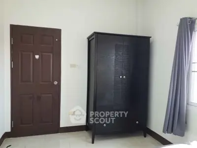 Minimalist bedroom with dark wardrobe and brown door, featuring natural light from window.