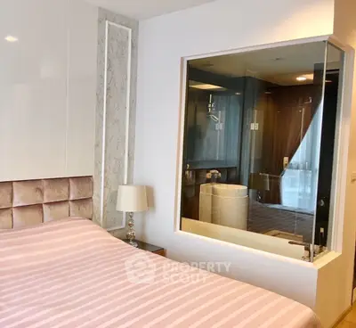 Modern bedroom with unique glass wall view into bathroom, featuring elegant decor and soft lighting.