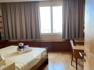 Cozy bedroom with wooden flooring and large window, featuring a comfortable bed and study desk.