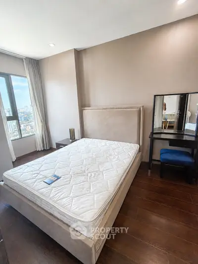 Spacious bedroom with large window offering city views, featuring a comfortable bed and elegant vanity set.