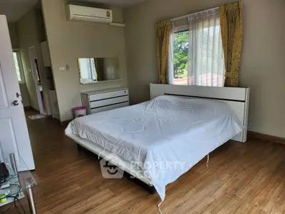 Spacious bedroom with wooden flooring and large window offering natural light.