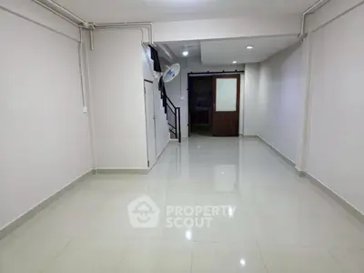 Spacious empty room with glossy tiled flooring and staircase access