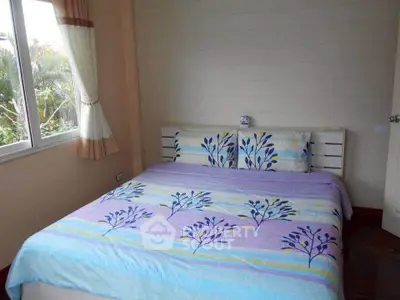 Cozy bedroom with floral bedding and large window offering natural light.