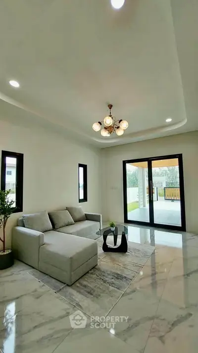 Elegant living room with modern sofa and chandelier, opening to a spacious balcony with garden view.