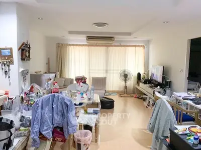 Spacious living room with cluttered furniture and natural light