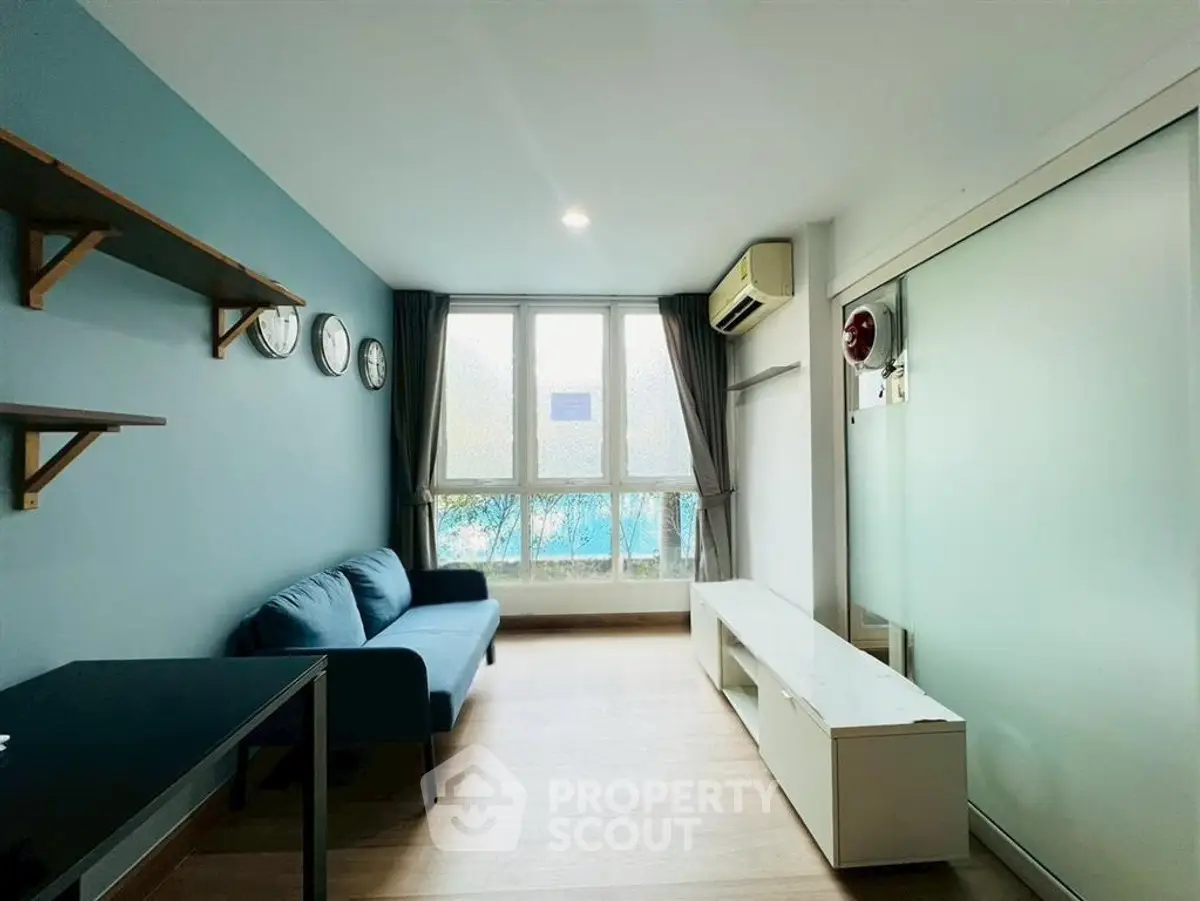 Modern living room with blue sofa, wall-mounted shelves, and large window for natural light.