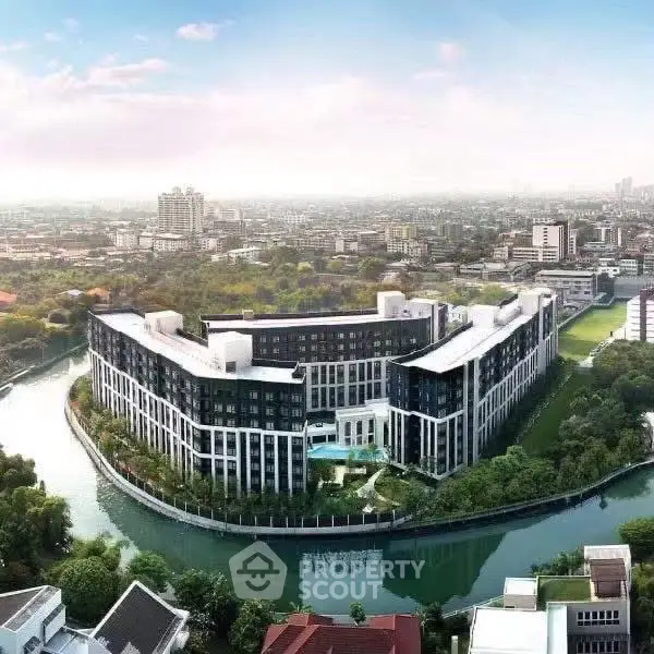 Stunning aerial view of modern riverside apartment complex with lush greenery and cityscape backdrop.