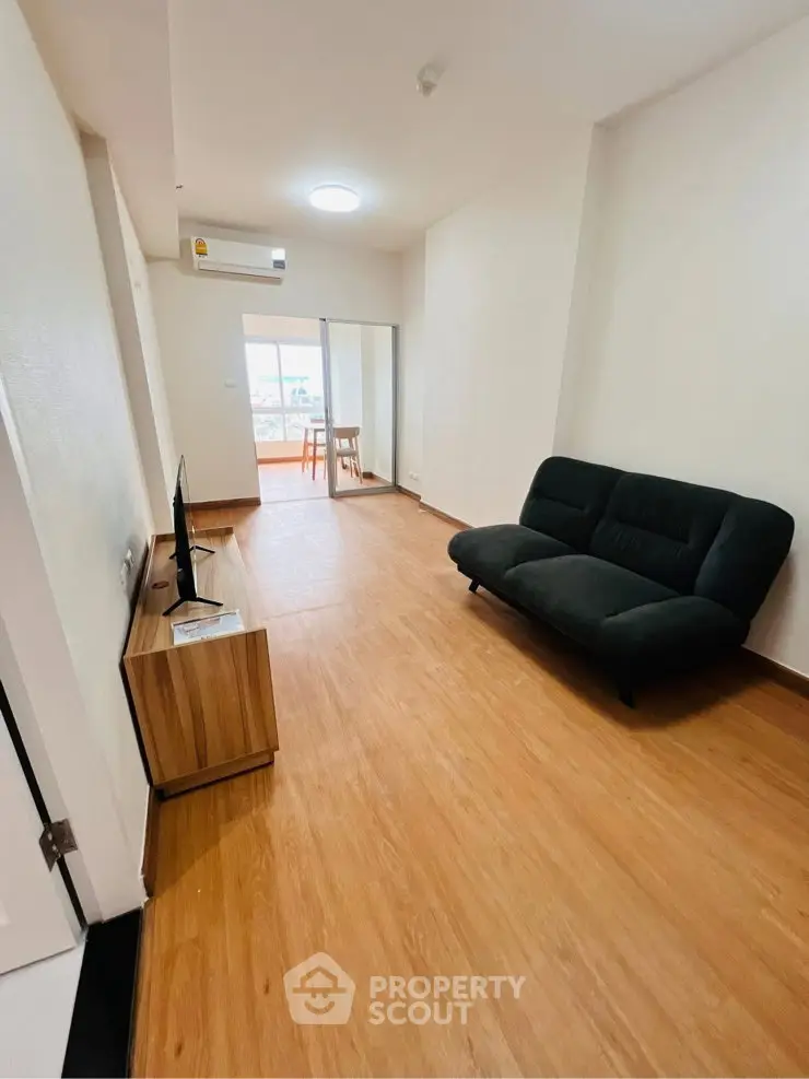 Modern living room with sleek wooden flooring and stylish furniture, leading to a bright balcony view.