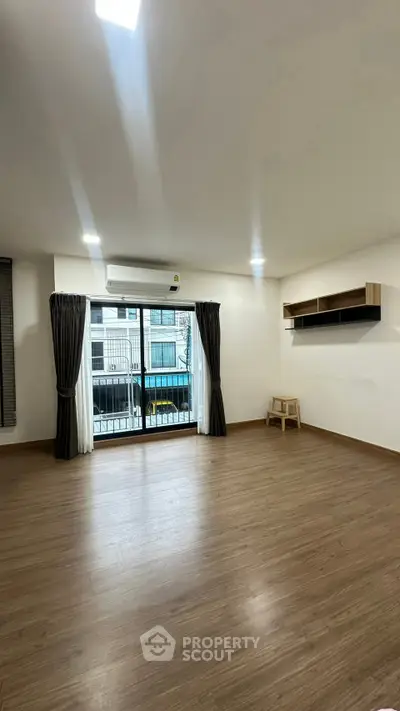 Spacious empty living room with large window and wooden flooring