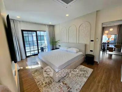 Spacious bedroom with modern decor and balcony access, featuring elegant lighting and hardwood floors.