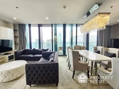 Luxurious open-plan living space with plush seating, elegant dining area, and a stunning chandelier, leading to a sunlit balcony with a view.