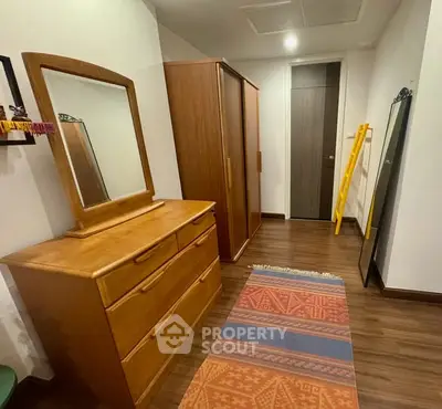 Spacious bedroom with wooden furniture and colorful rug, offering ample storage space.